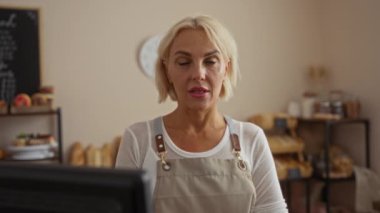 Fırında çalışan bir kadın önlük giyiyor. Etrafı ekmek ve hamur işleriyle çevrili.