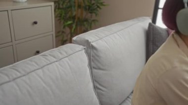 Kısa saçlı güzel bir kadın evdeki rahat bir oturma odasında, kulaklıklı bir kanepede dinleniyor..