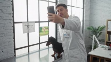 Klinikteki genç bir İspanyol erkek veteriner muayene masasında bir köpekle video görüşmesi yapıyor ve profesyonel bir çalışma alanını gösteriyor..