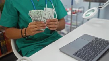 Genç İspanyol erkek veteriner veteriner veteriner kliniğinde Amerikan dolarlarını sayıyor, yeşil önlük giyiyor, etrafı tıbbi ekipman ve kitaplarla çevrili,.