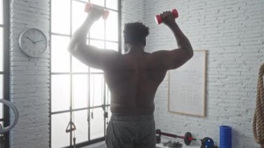 Spor salonunda ağırlık çalışan genç bir erkek, kapalı bir spor merkezinde güçlü sırt kaslarını ön plana çıkarıyor..