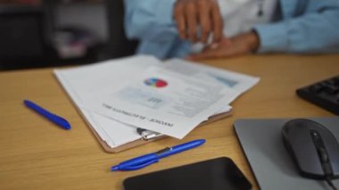 Ofis ortamında evrakları ve faturaları inceleyen Afro-Amerikalı genç bir adam, çeşitli ofis malzemeleri ve ekipmanların bulunduğu bir iş yeri ortamı sunuyor..