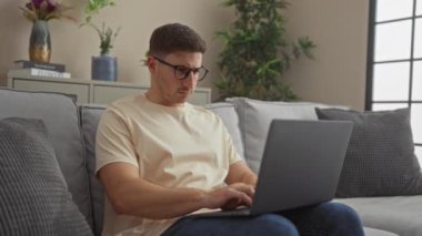 Evde dizüstü bilgisayar kullanan genç bir İspanyol 'un gizli çekimleri. Oturma odasında gözlüklerini çıkarırken odak ve yorgunluk anları sergiliyor..