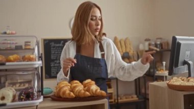 Kadın pastanede çalışıyor, pastane tezgahının arkasında hamur işlerini düzenliyor.