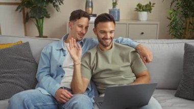 Oturma odalarındaki kanepede otururken bilgisayar başında video görüşmesi yapan eşcinsel bir çift.