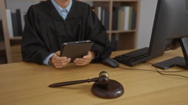 Yargıç cüppeli kadın ofis masasında tokmak ve bilgisayarla tablet kullanıyor, yasal ve hukuki süreci temsil ediyor, resmi bir ortamda çalışırken.