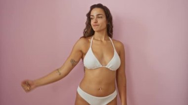 Kaslı, gururlu, bikinili, kollarını esneten İspanyol bir kadın izole edilmiş pembe arka plan fitness ve güç konsepti üzerinde. 