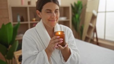 Kaplıcada aromatik mumu seven bir kadın, rahatlama ortamında beyaz bornoz giyer. Kapalı alanda yeşillik ve güzellik deneyimi için sakin bir ortam.
