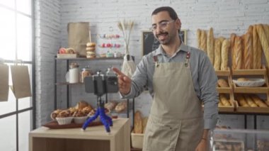 Önlüklü genç adam ekmek ve hamur işleri sergilerken fırında canlı yayın yapıyor. Arka planda fırınlanmış gıdalar ve tripoda yerleştirilmiş akıllı telefonlar var.