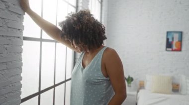 Yatak odasındaki pencereye yaslanmış kıvırcık saçlı ve evde başı dönen bir kadın.