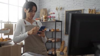 Pasta ve ekmekle çevrili şık fırında akıllı telefon kullanan bir kadın.
