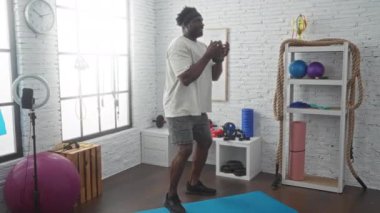 Genç bir Afrikalı Amerikalı spor salonunda egzersiz yapıyor. Kettlebell, direniş bantları ve yoga topu gibi spor aletleriyle çevrili..