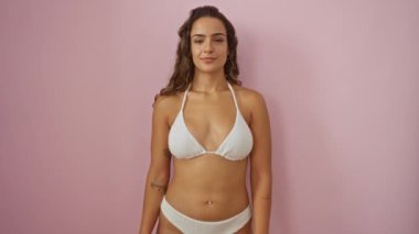 Bikinili genç İspanyol kadın, izole edilmiş pembe arka planda başarılı bir iş anlaşması için dostça el sıkışma teklif ediyor.