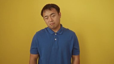 Üzgün ve bunalımlı genç Çinli adam. Kızgın ve endişeli bir ifadeyle izole edilmiş sarı arka planda duruyor. Sıkıntılı bir şekilde ağlıyor ve stresten korkuyor.