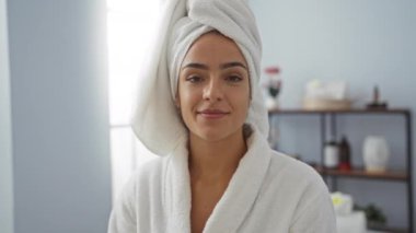 Spa Sağlık Merkezi 'nde bornoz ve havlu giyen genç bir kadın. Rahatlamış ve mutlu bir ifadeyle yüz bakımından zevk alıyor.