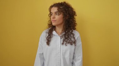 Sade doğal yüzünde gevşek ve ciddi bir ifadeyle duran tişört giyen genç İspanyol kadın izole edilmiş sarı bir arka plandan kameraya bakıyor.