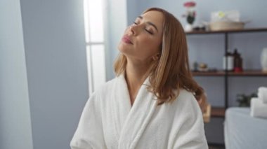 Genç bir kadın bornozla sağlık kaplıcasında dinleniyor, sakin bir atmosferi olan bir güzellik merkezinde huzurlu anların tadını çıkarıyor.