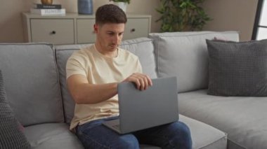 Genç bir İspanyol evdeki dizüstü bilgisayarda çalışıyor. Oturma odasındaki rahat bir kanepede oturuyor..