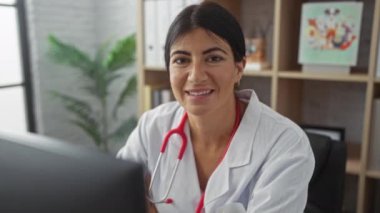 Klinikte kolları çaprazlanmış, steteskop takmış ve içeride gülümseyen İspanyol bir kadın doktor..