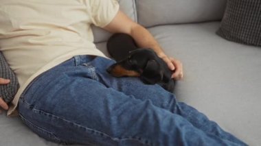Oturma odasındaki kanepede uyuyan genç bir adam kucağında küçük bir köpek dinleniyor..