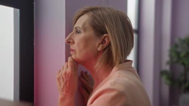 Evinin penceresinden içeri bakan orta yaşlı bir kadın düşünceli bir ifadeyle, yüzünü aydınlatan bir polis arabasının ışığıyla..