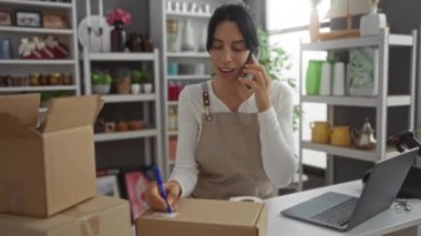 Dekorasyon malzemeleri ve dizüstü bilgisayarla çevrili ev dekorasyon mağazasında telefonla konuşurken kadın ambalaj kutusu