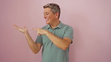 Kafkasyalı adam şaşırmış ve gülümsüyor. Elle sunarken ve izole pembe arka planı işaret ederken.