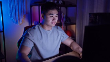 Geceleyin loş bir odada bilgisayar üzerinde çalışan Asyalı genç bir adam..