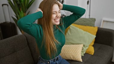 Sarışın kadın neşeli bir şekilde modern bir koltukta renkli yastıklarla oturma odasında gülüyor.