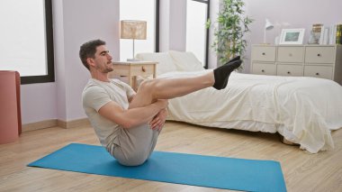 Genç bir adam minimalist bir yatak odasında mavi bir paspasın üzerinde egzersiz yapıyor, modern ve sağlıklı bir yaşam tarzı sergiliyor..