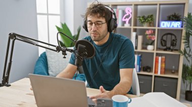 Modern bir stüdyo ortamında mikrofon ve kulaklıkla Hispanik adam podcast 'i.