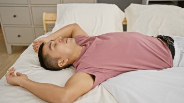 Genç İspanyol bir adam yatak odasında dinleniyor, huzurlu bir ifadeyle bir yatağa uzanıyor..