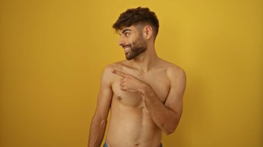 Çıplak göğüslü, sakallı, sırıtan genç bir adam izole edilmiş sarı arka planda dikilirken..