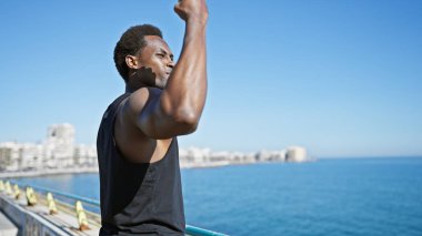 Açık mavi okyanusla güneşli bir sahil geçidinde uzanan Afrikalı Amerikalı bir adam.