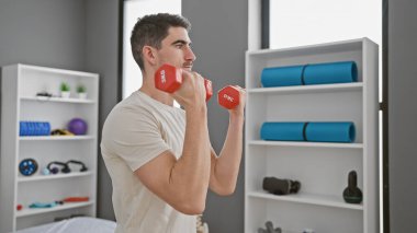 Modern bir rehabilitasyon merkezinde dambıllarla egzersiz yapan yakışıklı bir adam.