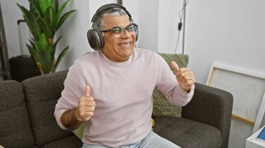 Neşeli orta yaşlı bir adam, rahat bir oturma odasında kulaklıkla müzik dinlemekten hoşlanır.