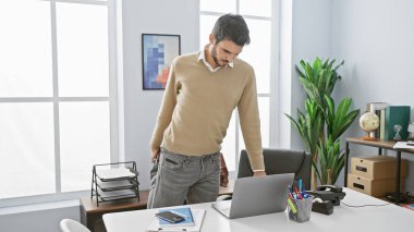 Parlak ofis ortamında dizüstü bilgisayarla çalışan yakışıklı İspanyol bir adam..