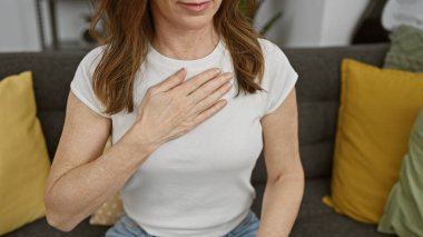 Orta yaşlı bir kadın, evin içinde yemin ediyor, samimiyeti çağrıştırıyor, rahat bir ev ortamında..