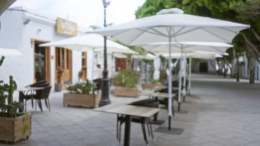 Güneşli bir günde açık hava kafeteryasında şemsiyeler, İspanya, çözülmüş masalar ve yeşil bitkiler..  