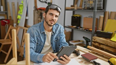 Yaratıcı bir marangozluk atölyesinde tablet kullanan yakışıklı bir zanaatkar.