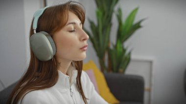 Rahat, genç, beyaz bir kadın huzurlu bir evde kulaklıklarla müzik dinlemekten hoşlanıyor.