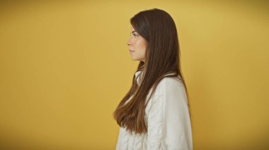 Sarı arka planda izole edilmiş, kendine güvenen genç bir İspanyol kadının profil portresi..