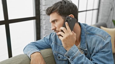 Kot pantolonlu yakışıklı adam telefonda, kanepede konuşuyor..