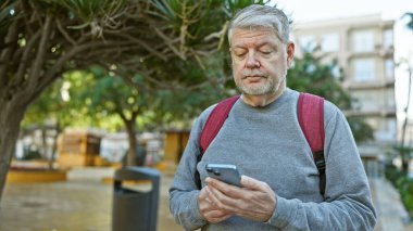 Gri saçlı olgun bir adam şehir sokaklarında akıllı telefon kullanıyor, şehir yaşam tarzı ve teknoloji kullanımı gösteriyor..