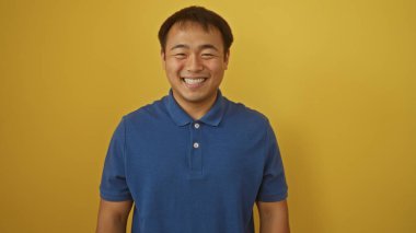 Mavi gömlekli yakışıklı genç Asyalı parlak sarı bir arka plana gülümsüyor..