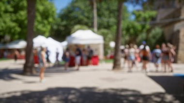 Güneşli bir günde, Mallorca 'da açık hava pazarının tadını çıkaran insanlar, dağılmış çadırlar, ağaçlar ve bokeh efektleri sergiliyorlar.