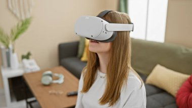 Sarışın kadın, oturma odasında sanal gerçeklik kulaklığı takıyor.