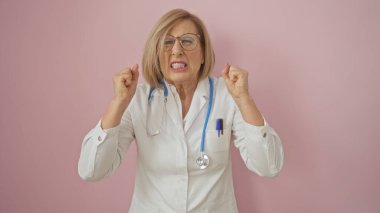 Beyaz önlüklü ve steteskoplu yaşlı beyaz bir kadın pembe arka planda tek başına dikilirken hayal kırıklığını ifade ediyor..
