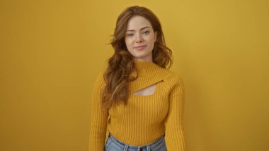 Attractive young blonde woman in a stylish yellow sweater posing confidently against an isolated yellow background wall. clipart