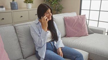 Genç, çekici, esmer bir kadın, rahat bir oturma odasında, rahat bir kanepe ve yumuşak yastıkla konuşuyor..